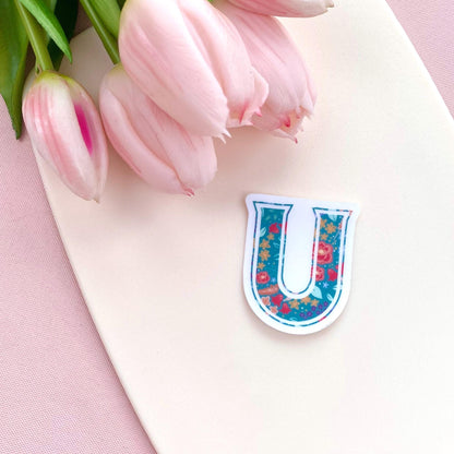 Colourful letter 'U' sticker with a floral pattern on a pink surface with pink tulips
