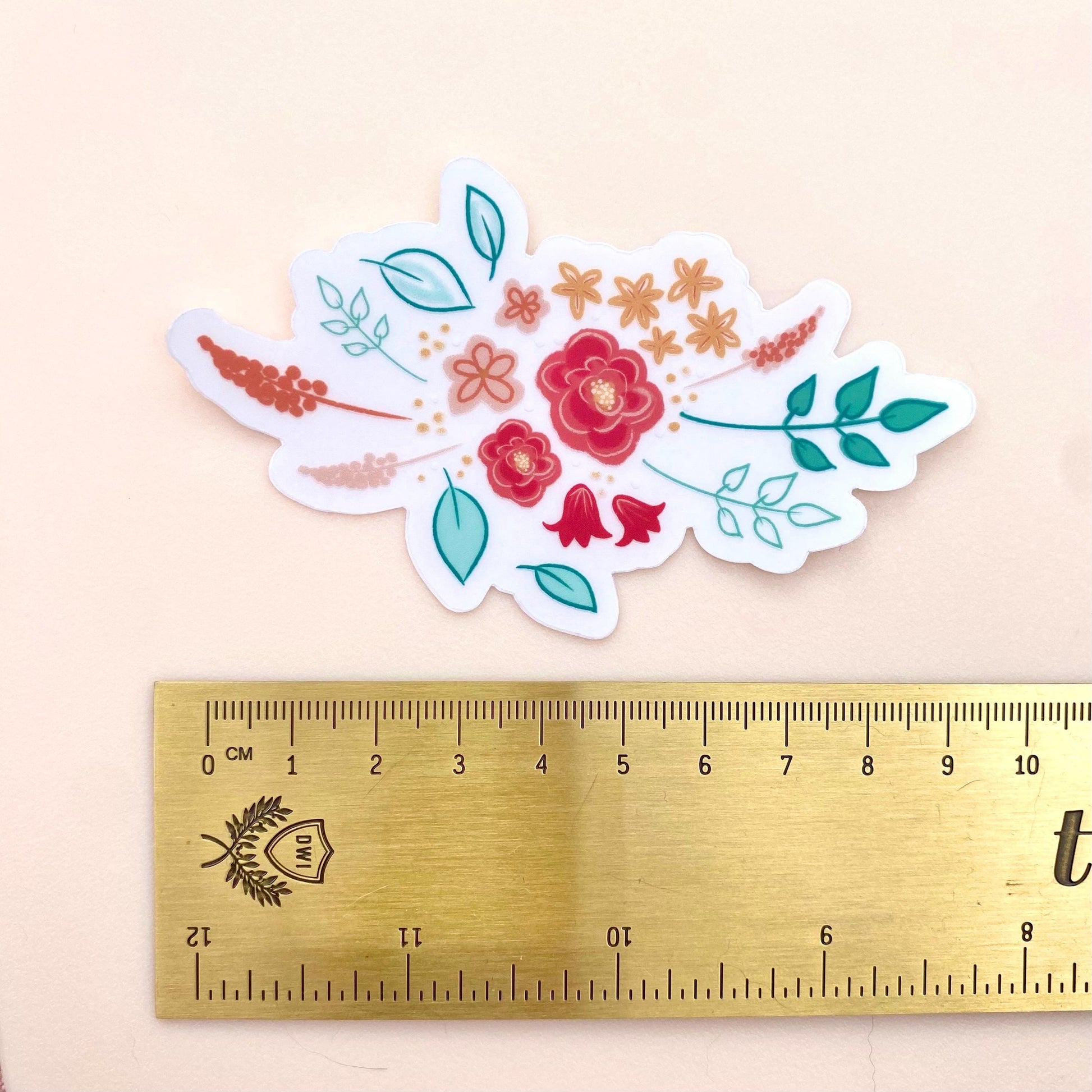Floral sticker with a gold ruler for scale on a beige background