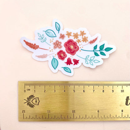 Floral sticker with a gold ruler for scale on a beige background