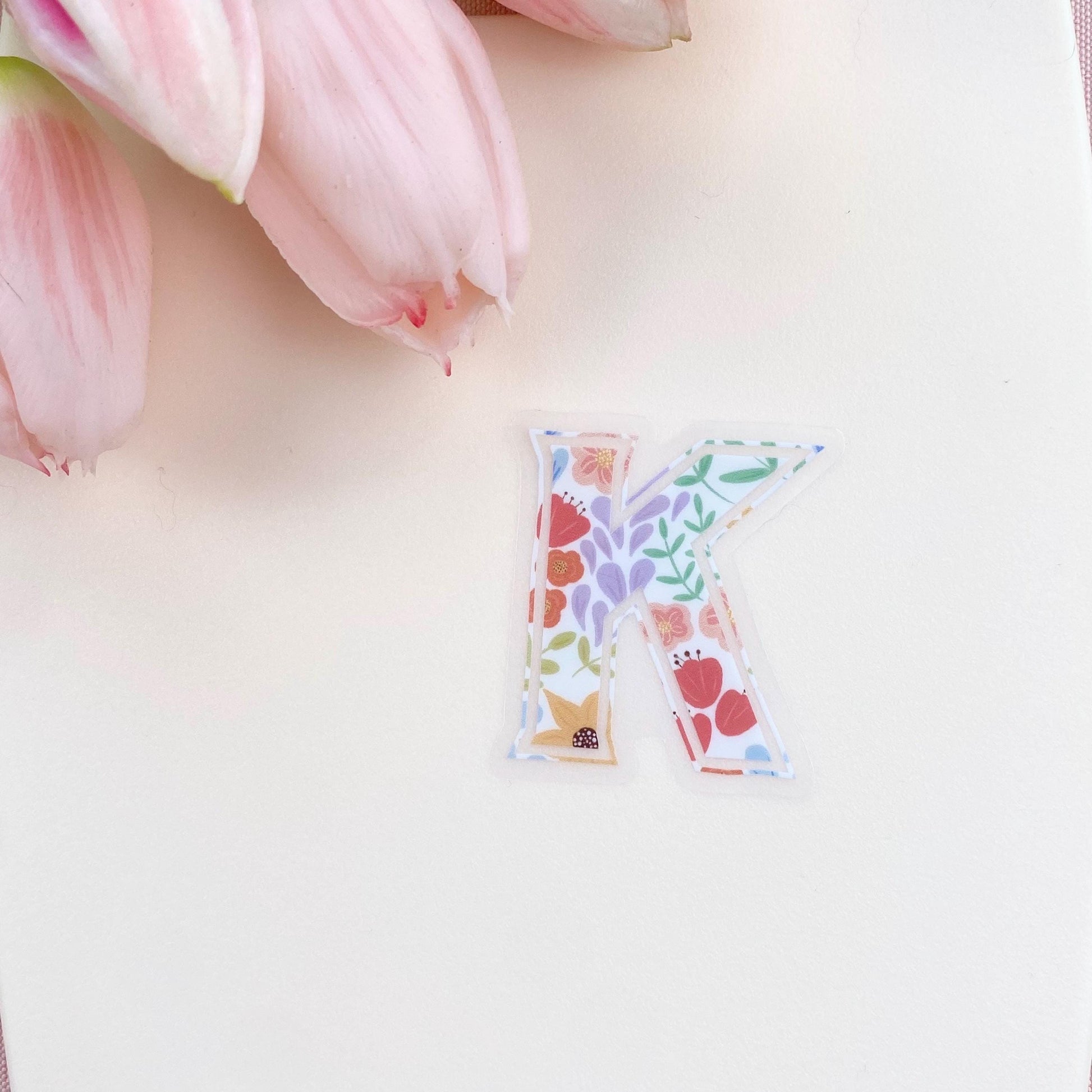 Colorful letter 'K' sticker on a light pink background with tulips