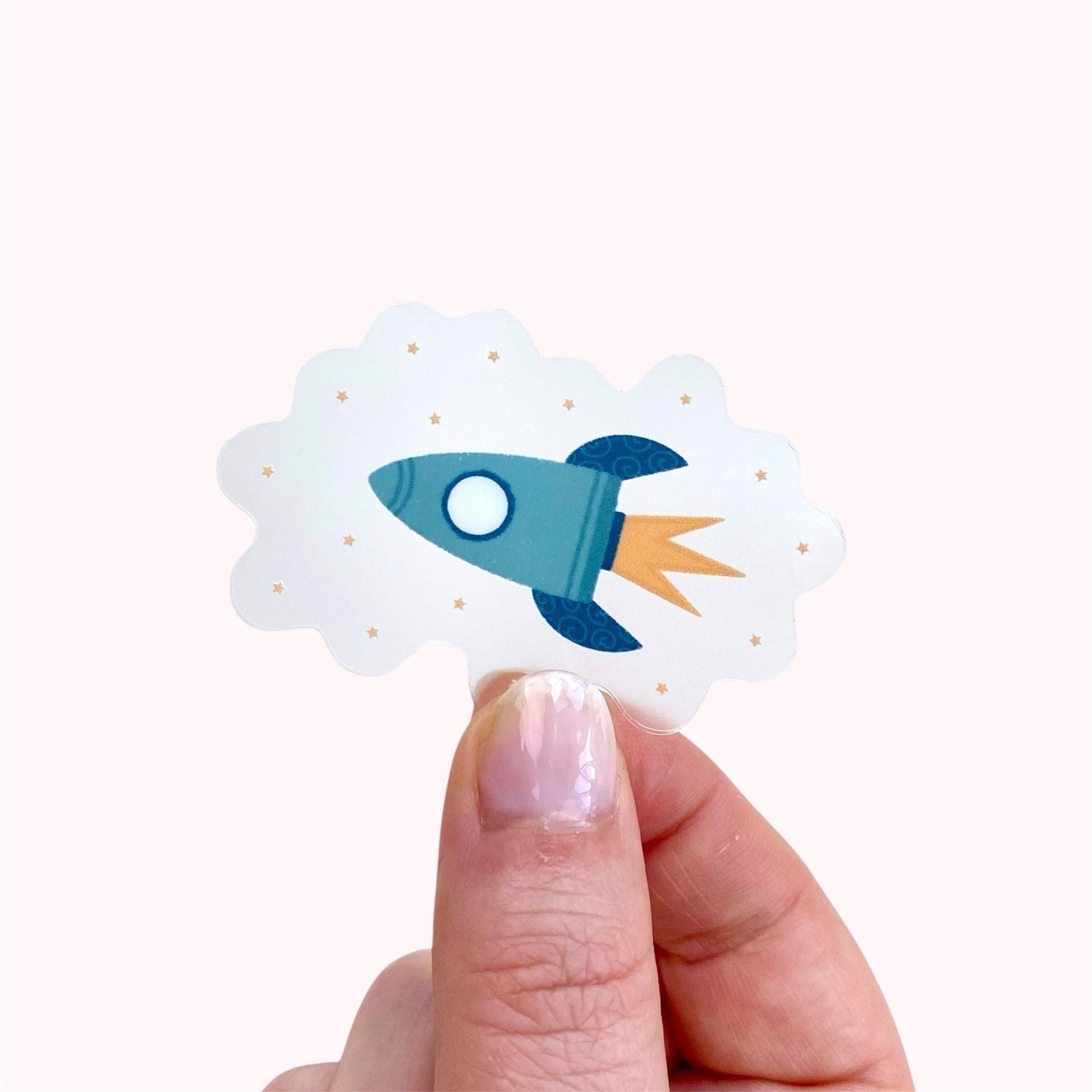 Hand holding a sticker of a blue rocket ship with a white background