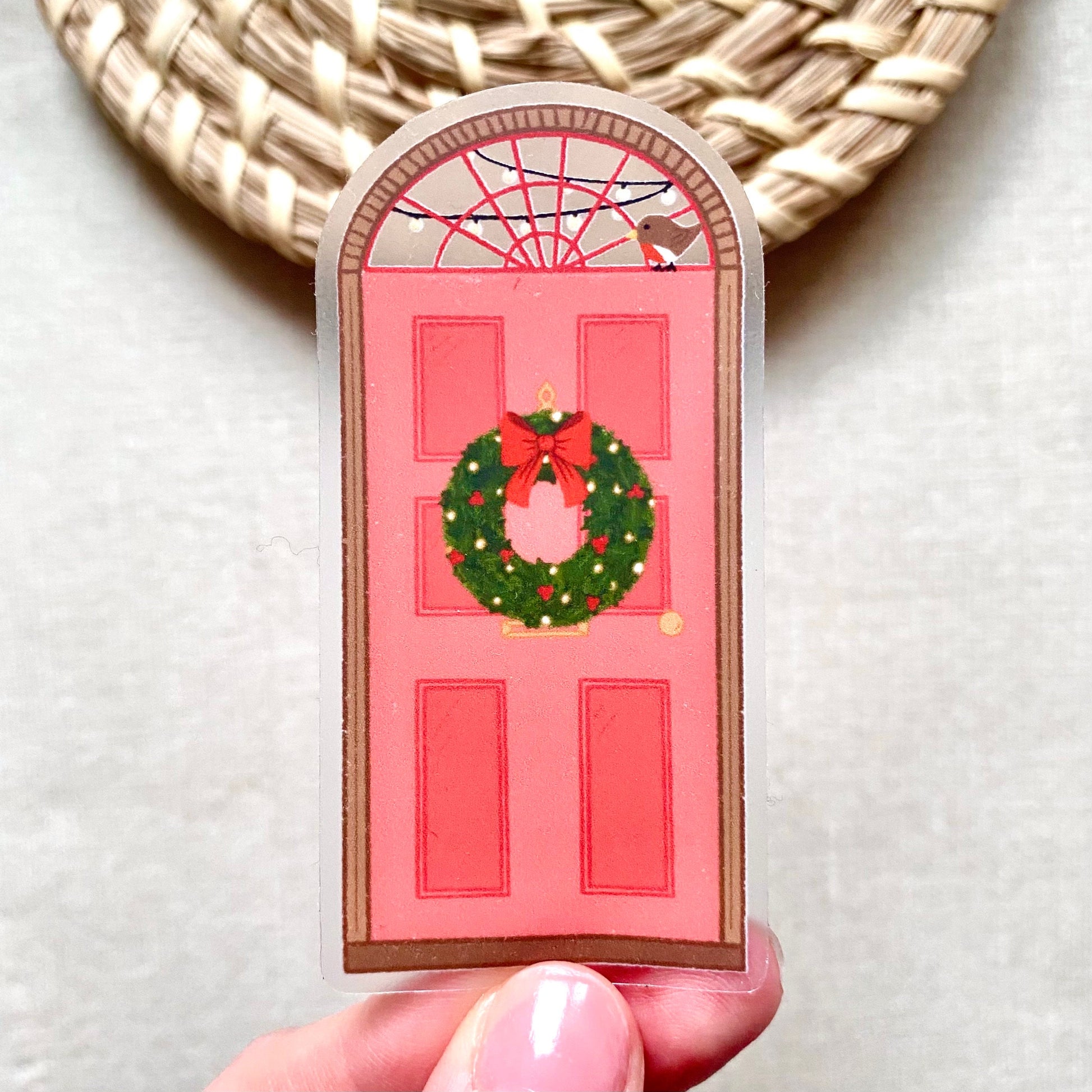 Decorative red door sticker with a wreath and bow held by a hand against a neutral background