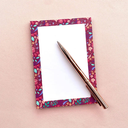 Floral-patterned notepad with a pen on a pink background
