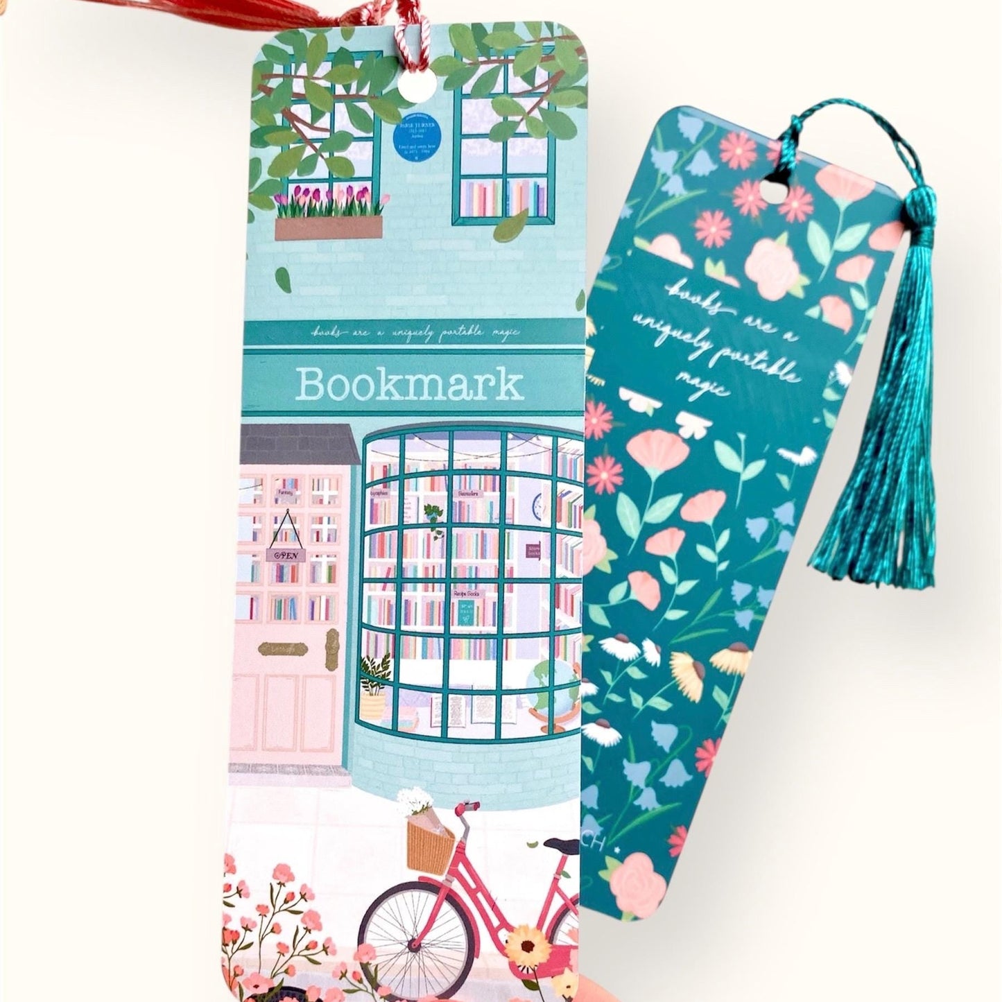 Two colourful bookmarks with tassels held by a hand against a white background, one showing the front and the other showing the back