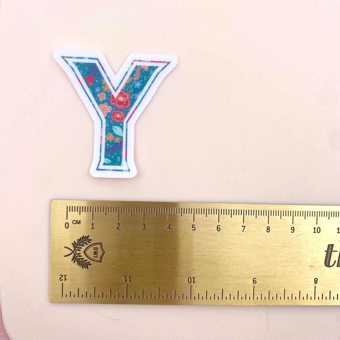 Floral letter 'Y' sticker next to a ruler on a pink background