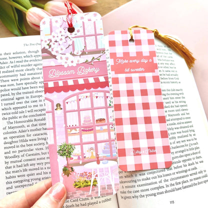 Two decorative bookmarks on a book with a pink and white checkered design and a bakery illustration.