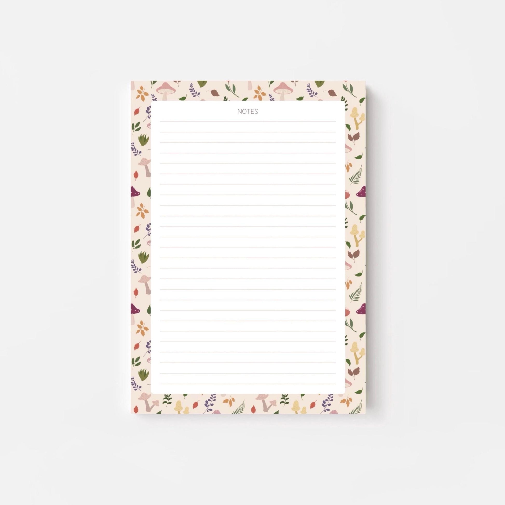 A lined notepad on a white background, with a beige border patterned with autumn leaves and mushrooms