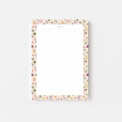 A lined notepad on a white background, with a beige border patterned with autumn leaves and mushrooms