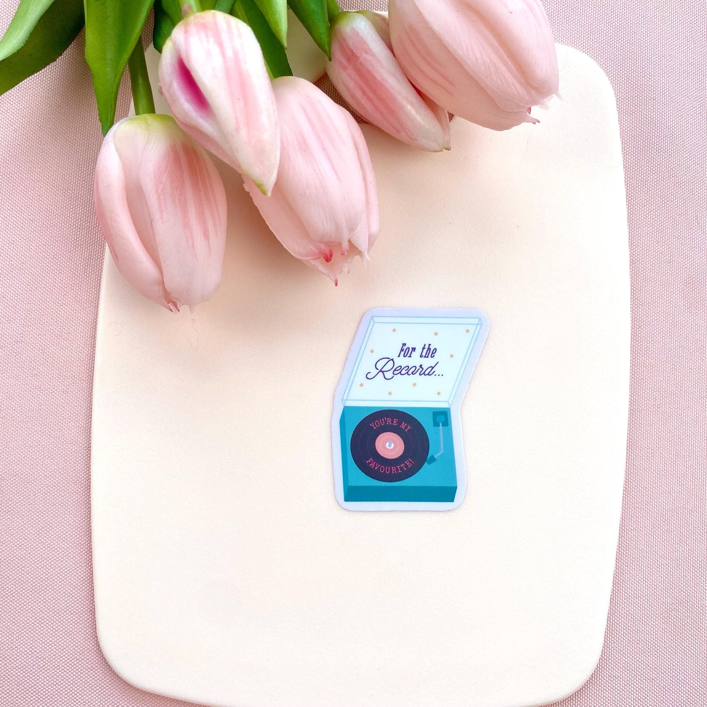 Pink tulips on a white surface with a blue record player sticker.