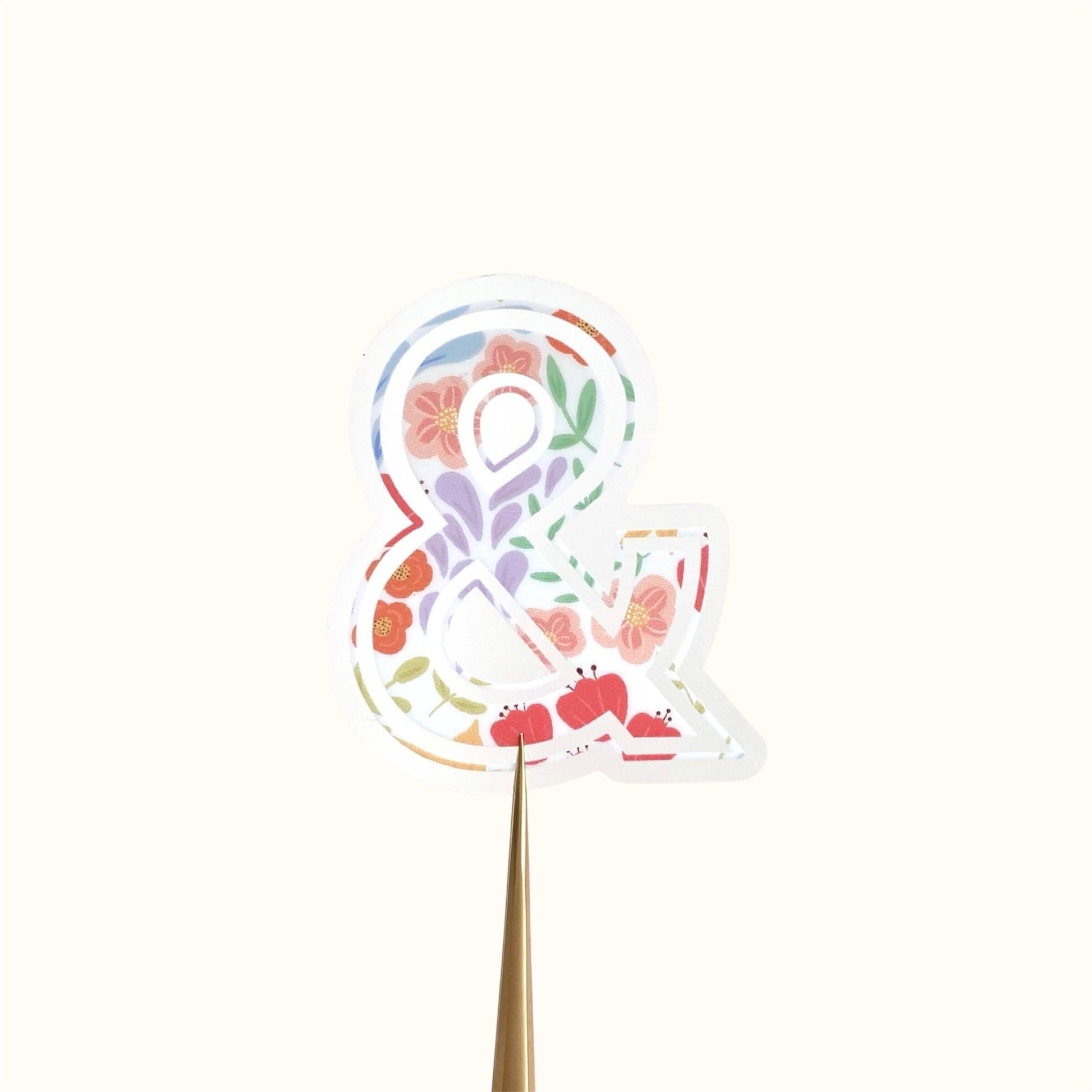 Decorative symbol'&' sticker with floral elements on a light pink background.