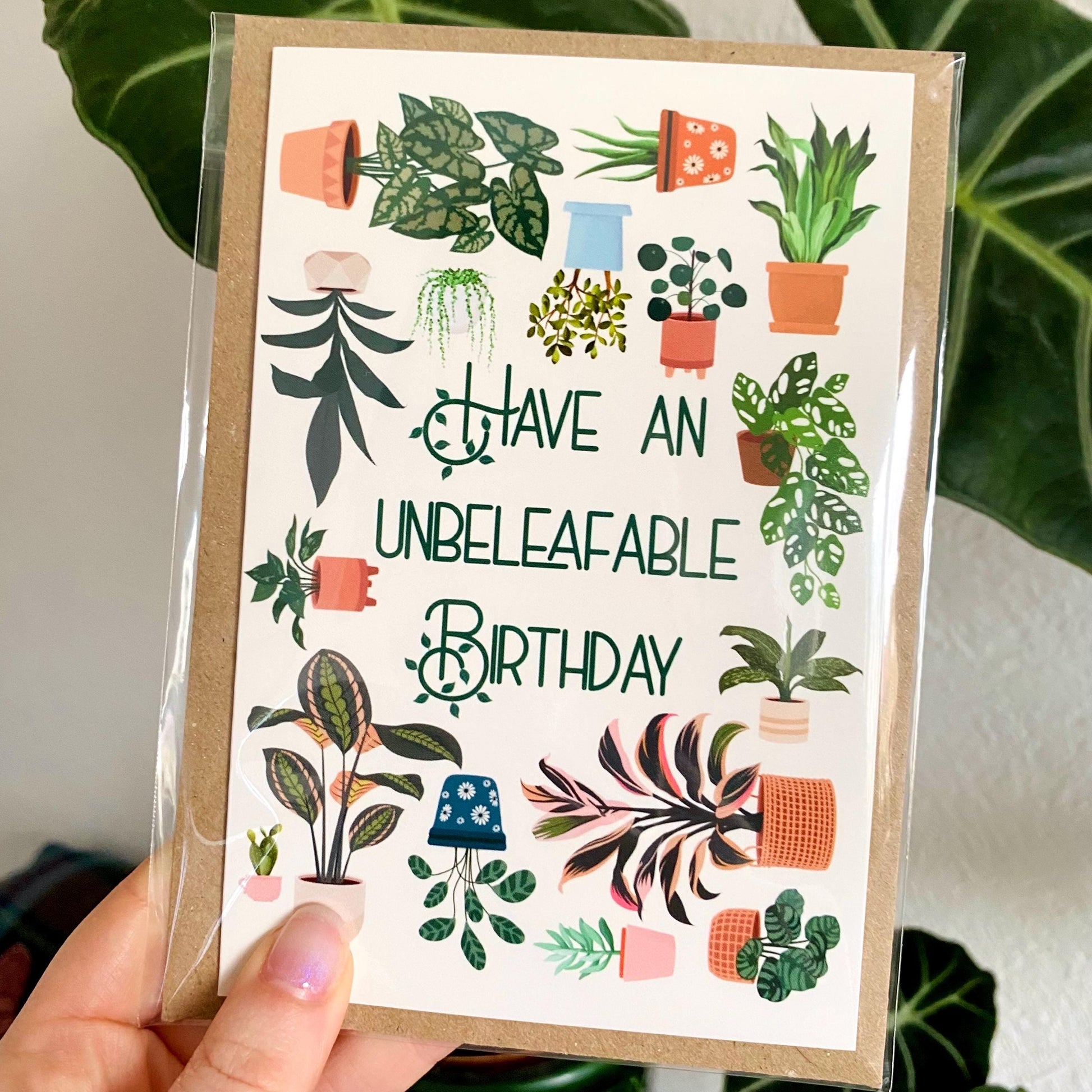 Greeting card with plant illustrations and text 'Have an unbeleafable birthday' held by a hand.