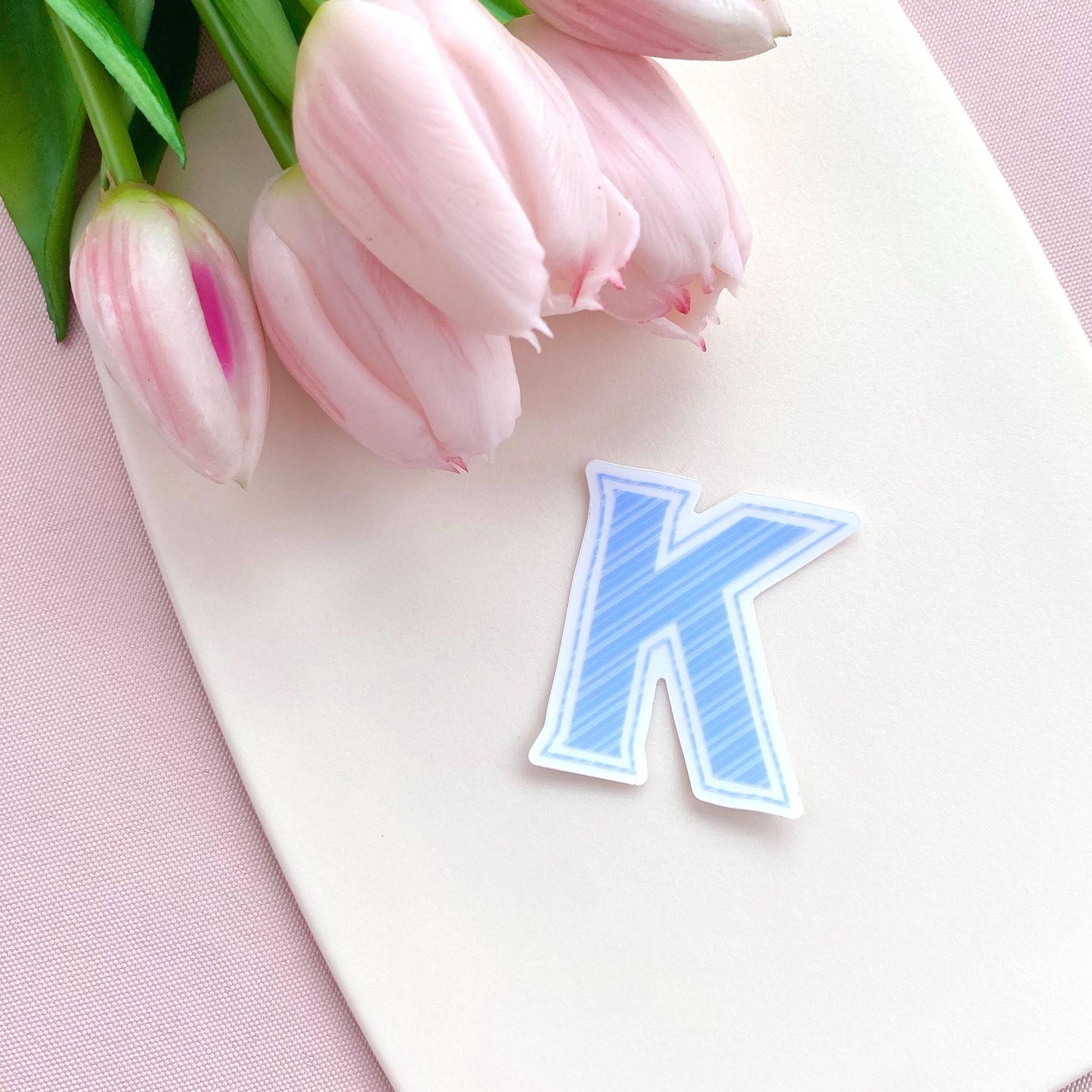 Blue striped letter 'K' transparent sticker against a white background with pink tulips