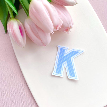 Blue striped letter 'K' transparent sticker against a white background with pink tulips