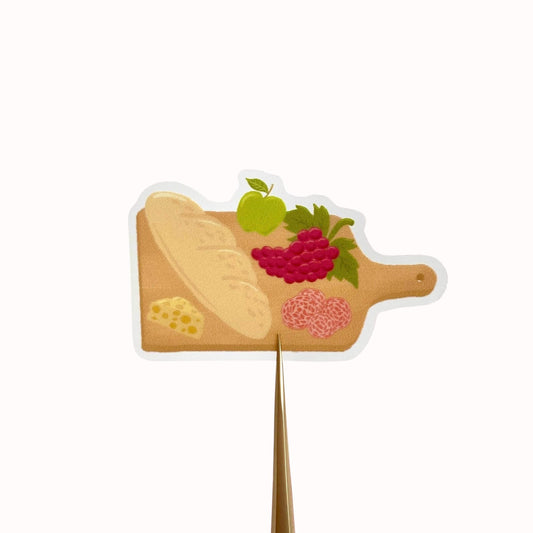Charcuterie board sticker with a baguette, cheese, grapes, apple and salami, against a cream background