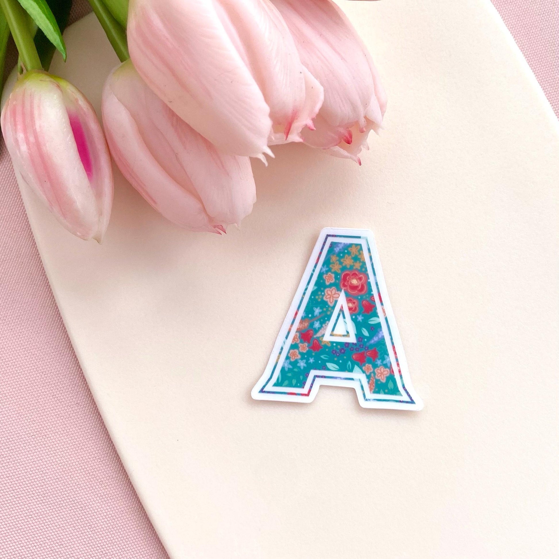 Floral letter 'A' sticker on a cream surface with pink tulips