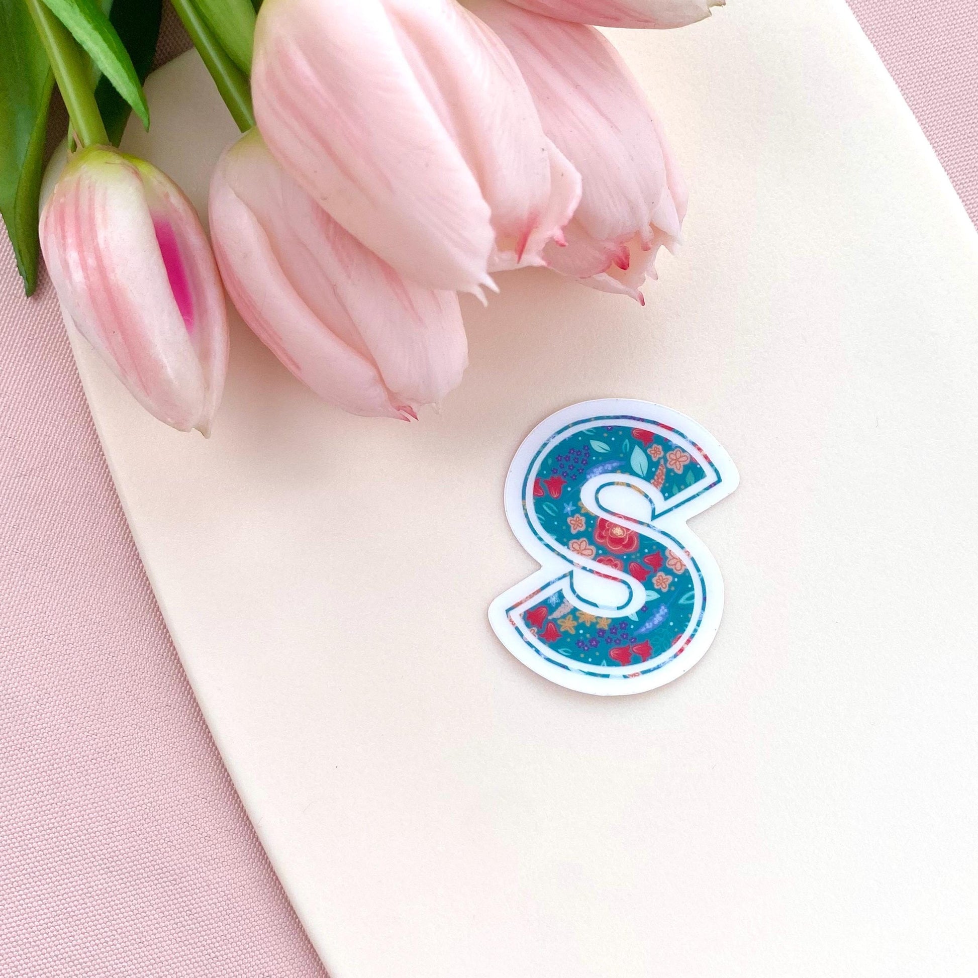 Floral letter 'S' sticker on a pink surface with pink tulips