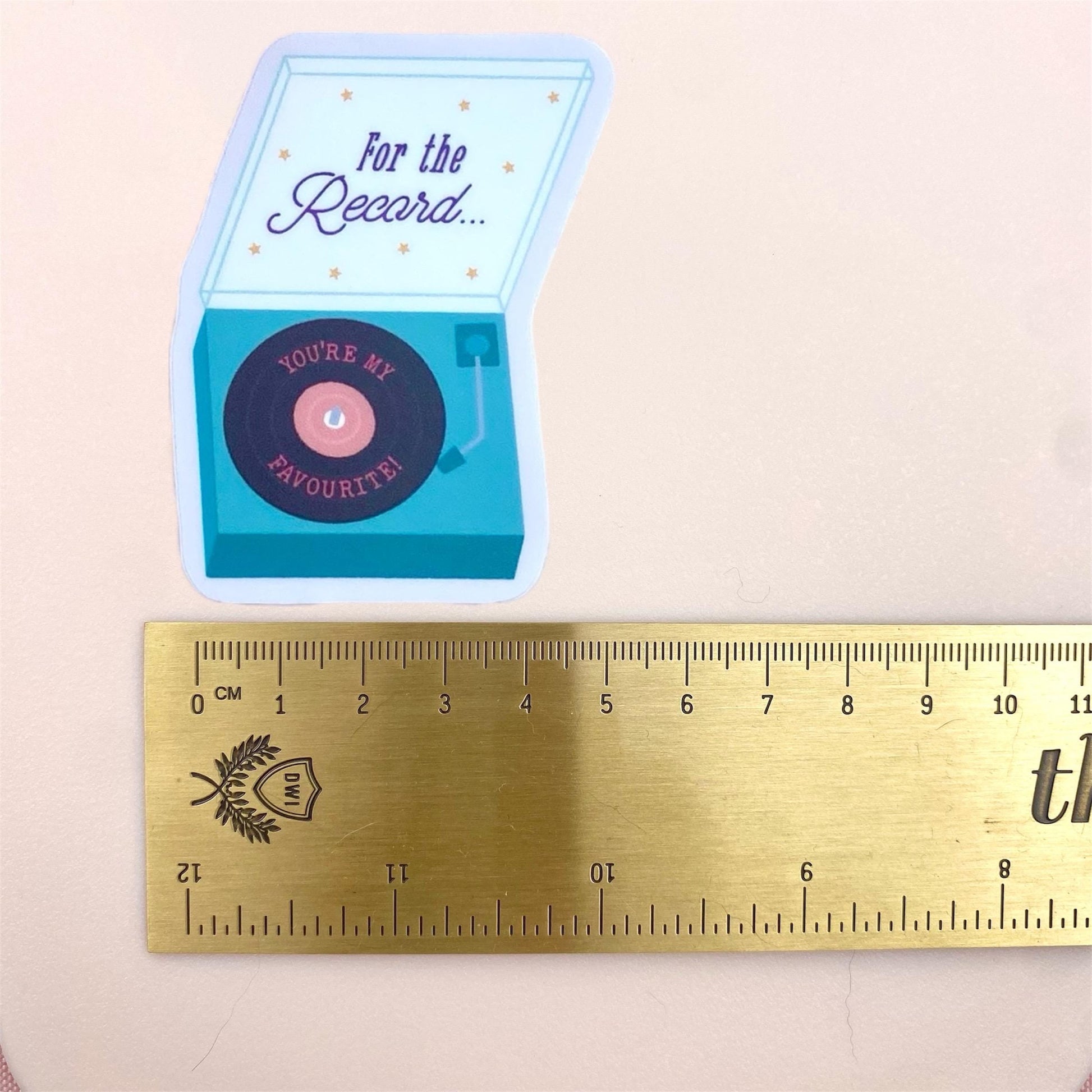 Small record player sticker with 'For the Record... you're my favourite' text next to a ruler for scale on a beige background