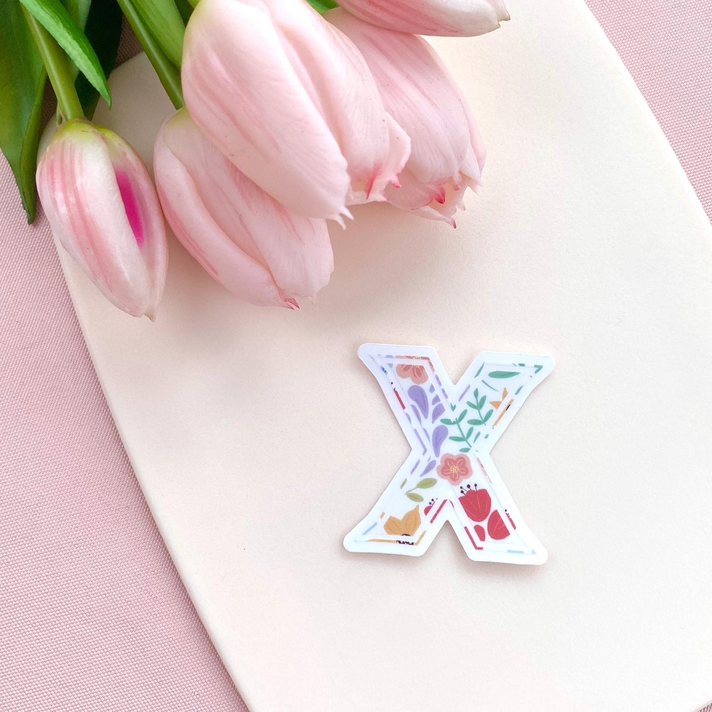 Decorative letter 'X' sticker with floral patterns on a pink surface with tulips.
