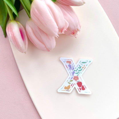 Decorative letter 'X' sticker with floral patterns on a pink surface with tulips.