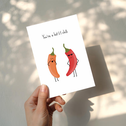 Card with cartoon red and orange  peppers and 'You're a hot li'l chilli' text held up by a hand against a white background