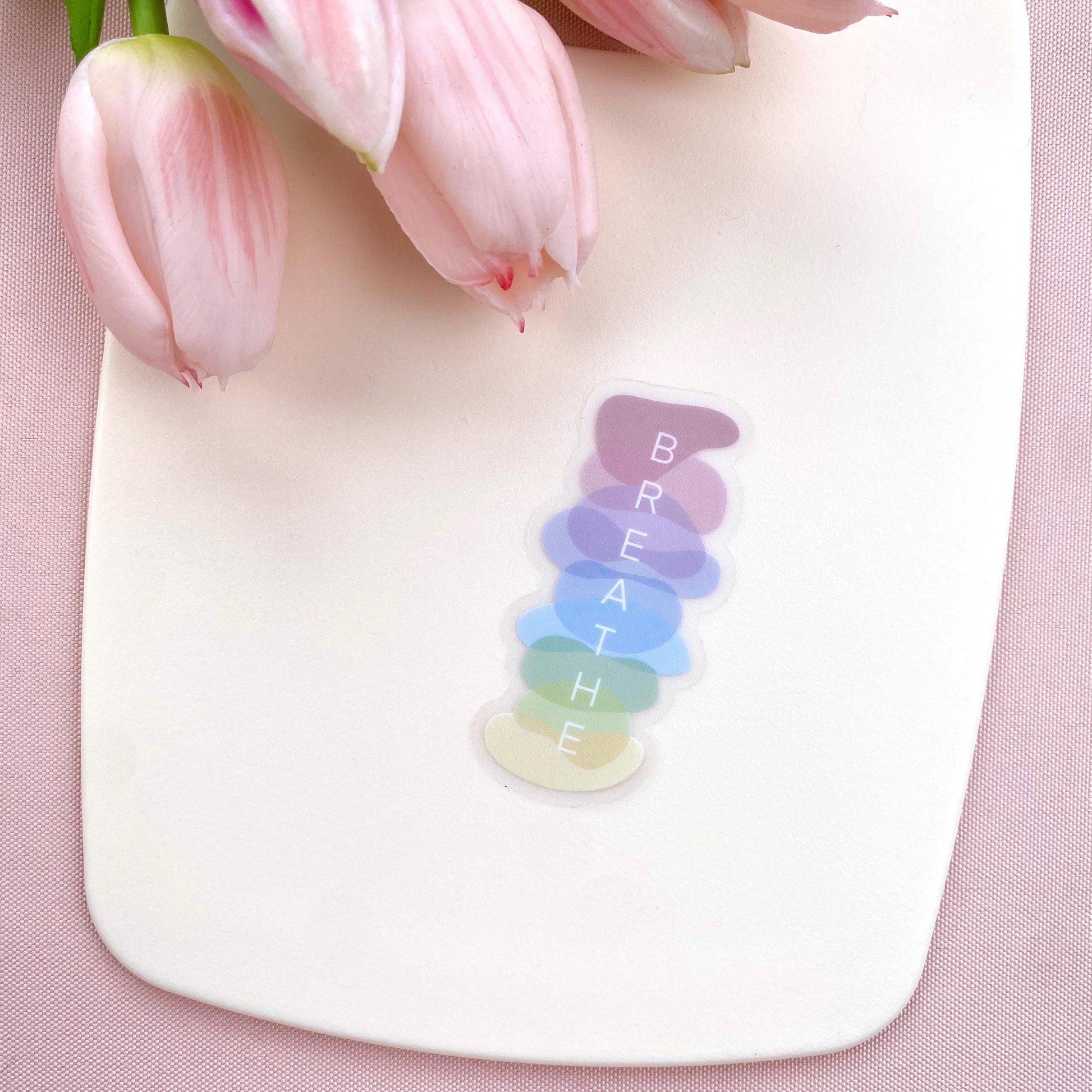 Colorful 'BREATHE' decal on a white surface with pink tulips in the background