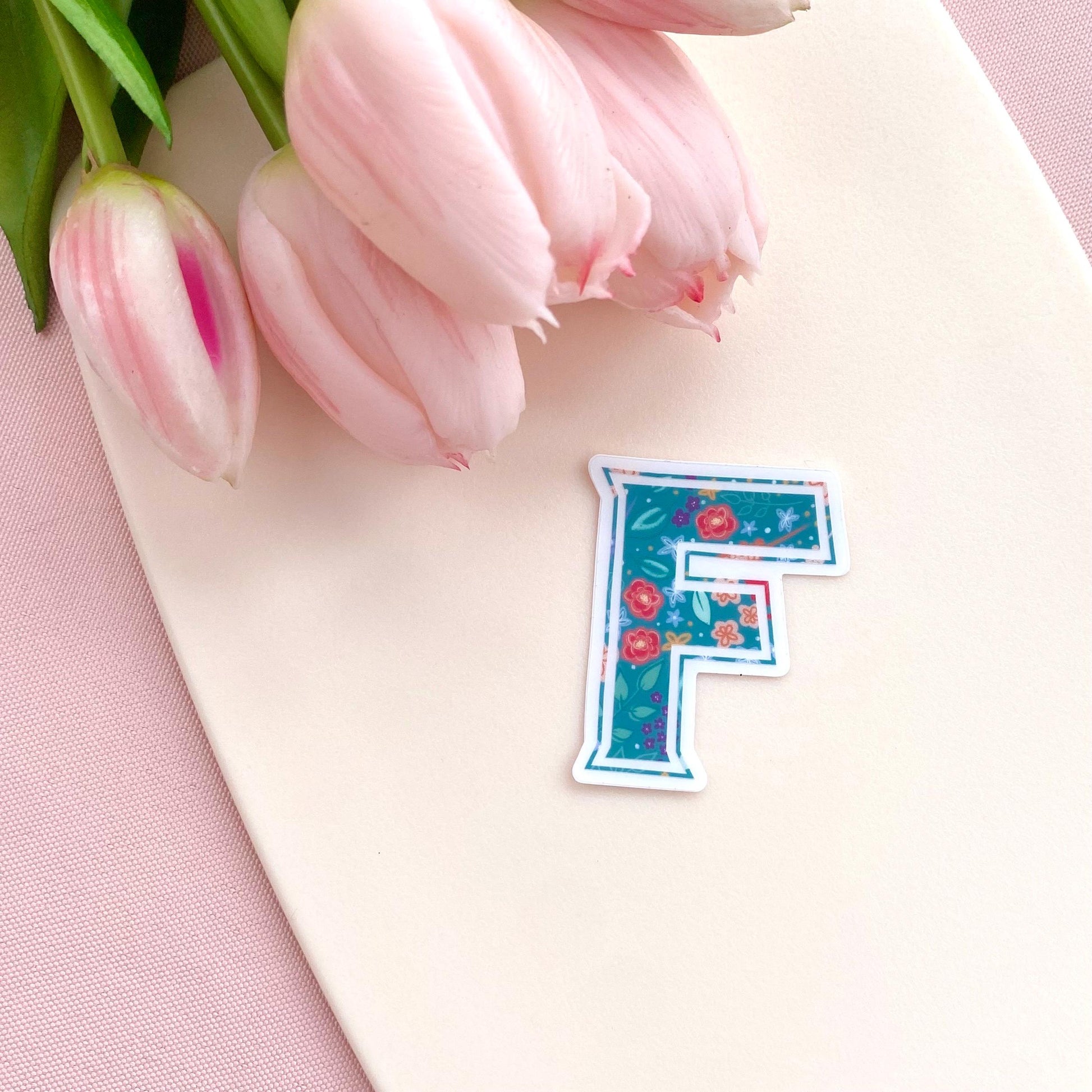 Floral letter 'F' sticker on a pink surface with tulips