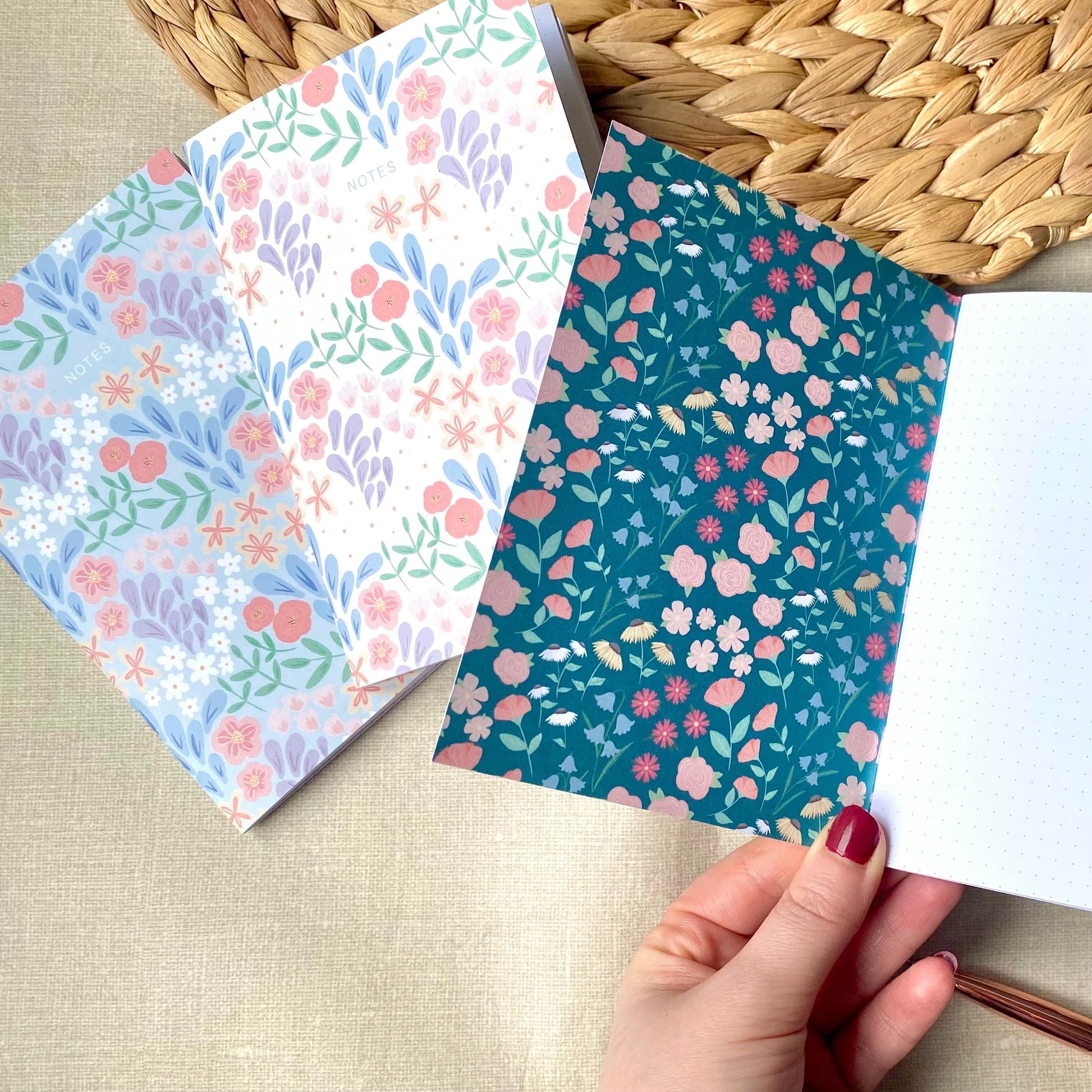 Two floral-patterned notebooks on a textured surface with a hand holding one of them.