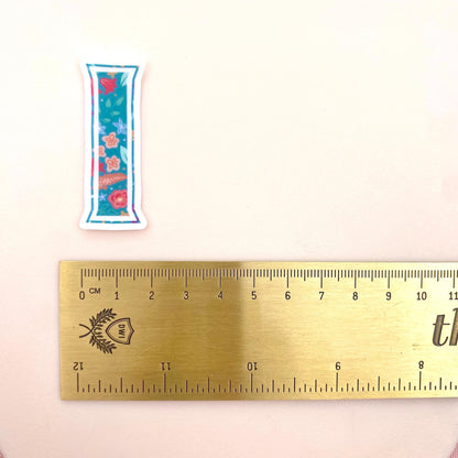 Clear vinyl sticker with a teal floral patterned letter 'I' shown on a white background with a gold ruler for scale