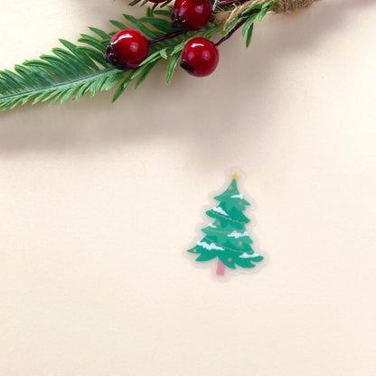 Small green Christmas tree sticker on a beige background with a branch of red berries and green leaves.