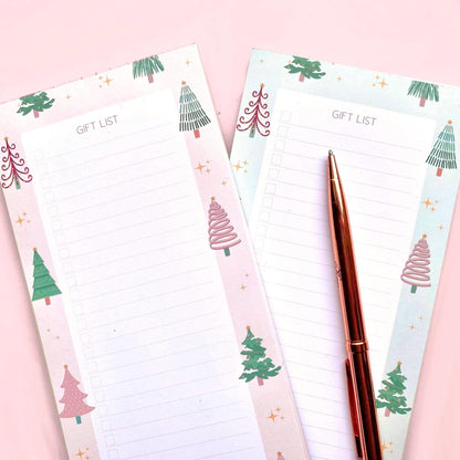 Note pads with Christmas tree designs and a pen on a pink background