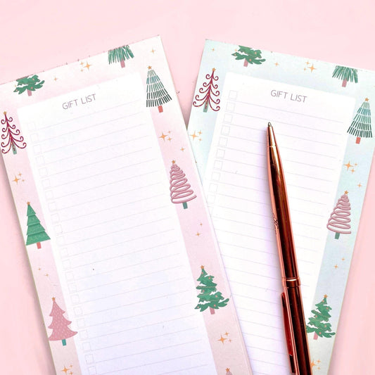 Note pads with Christmas tree designs and a pen on a pink background