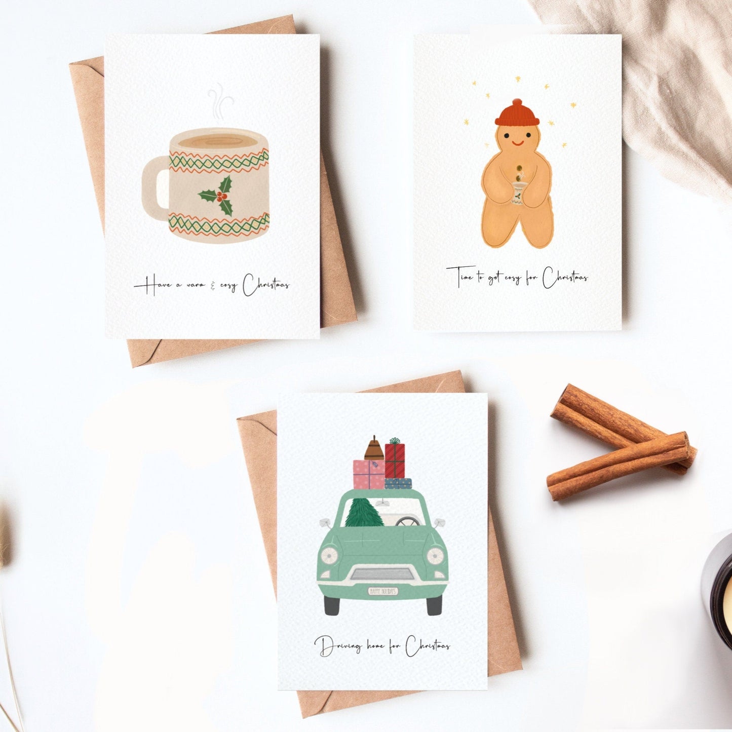 Set of Christmas-themed cards with envelopes on a white surface, featuring a mug, gingerbread man, and car with gifts.