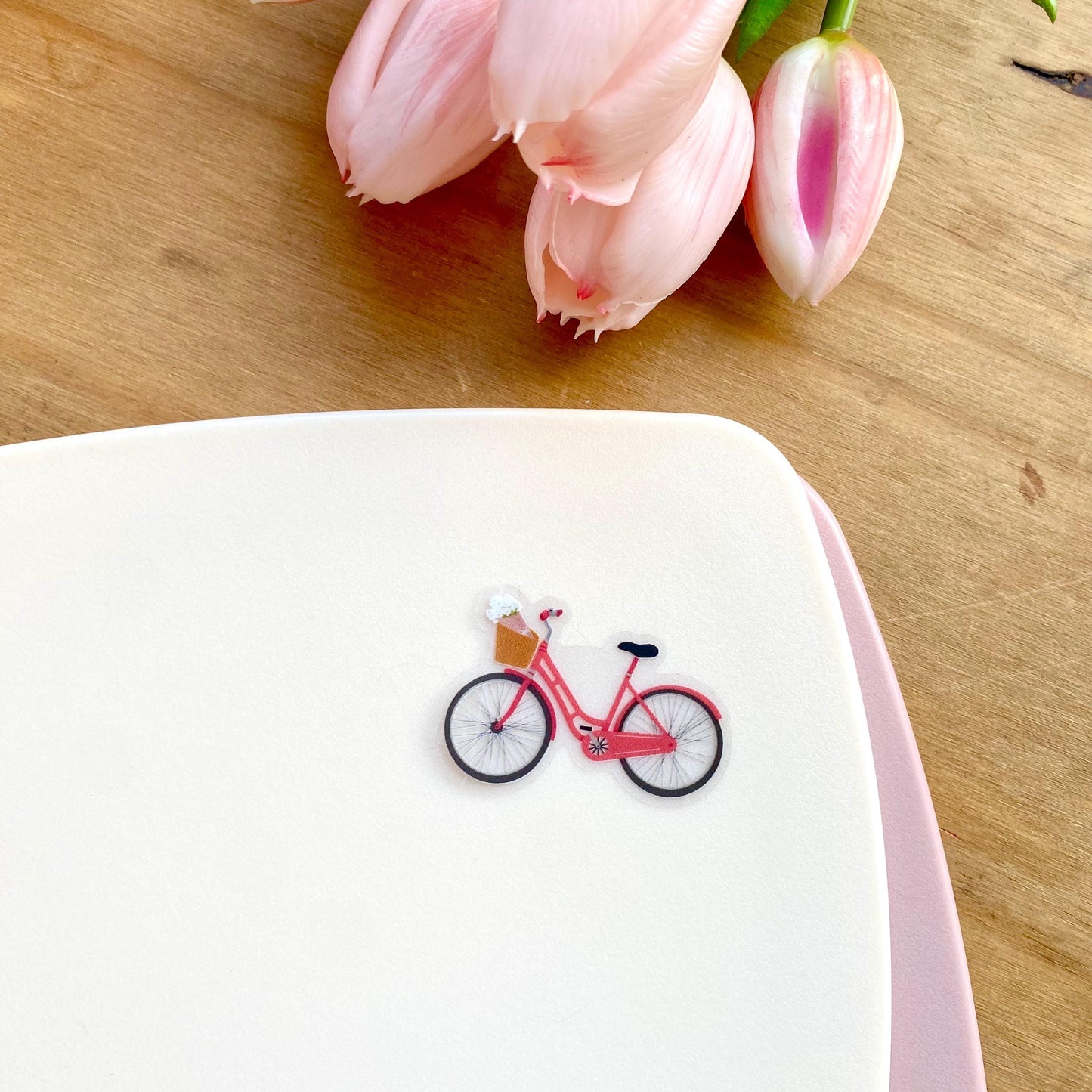 Pink bicycle sticker against a cream background with pink tulips.