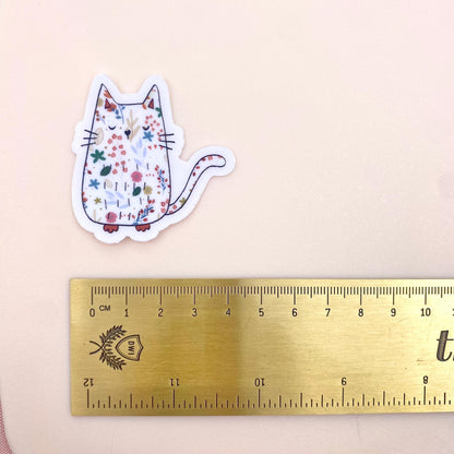 Sticker of a cat with floral patterns next to a ruler on a beige background