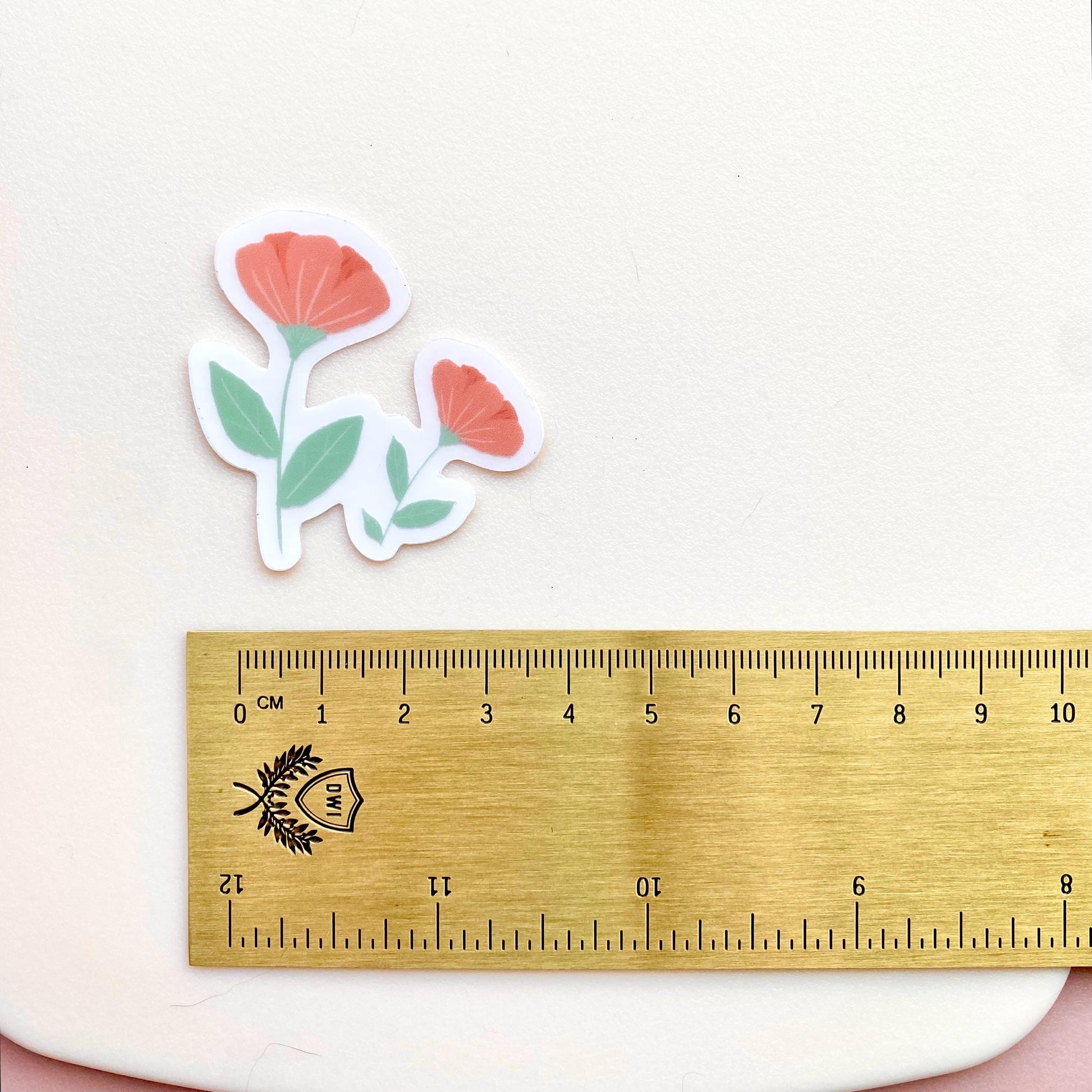Pink flowers sticker against a cream background with a gold ruler for scale.
