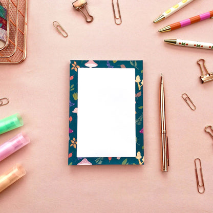 Notepad with mushroom and leaf patterned border on a white background with stationery items