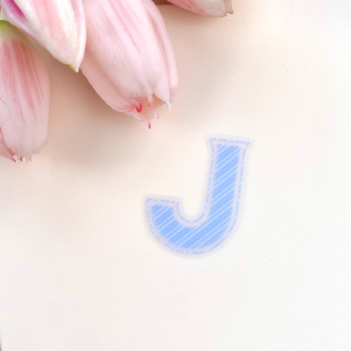 Blue striped letter 'J' sticker on a light pink background with tulips