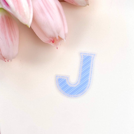 Blue striped letter 'J' sticker on a light pink background with tulips