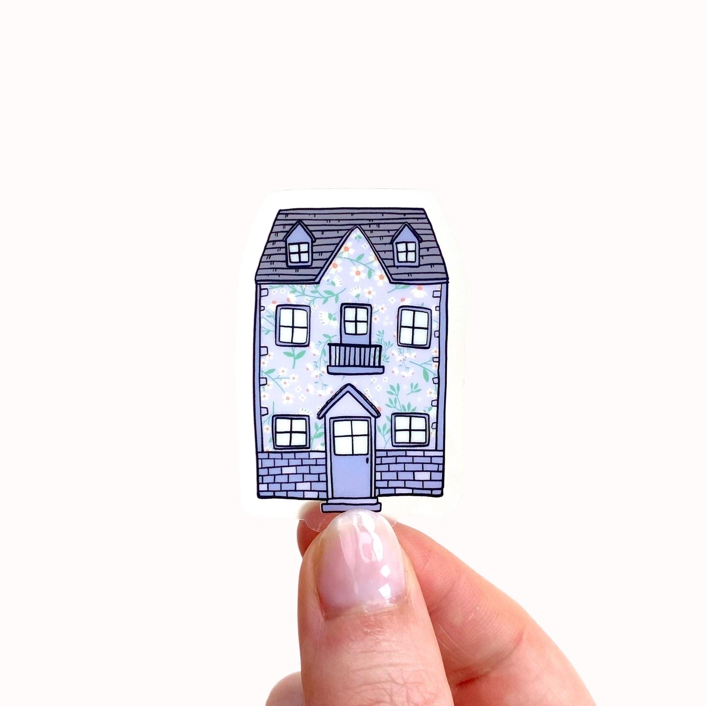 Purple floral patterned house sticker held between fingers on a white background