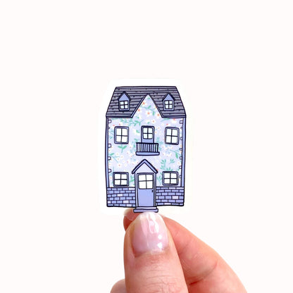 Purple floral patterned house sticker held between fingers on a white background