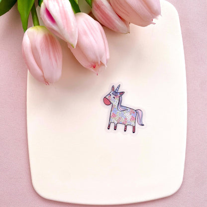 Floral patterned pink and blue unicorn on a transparent vinyl sticker against a white back ground with pink tulips