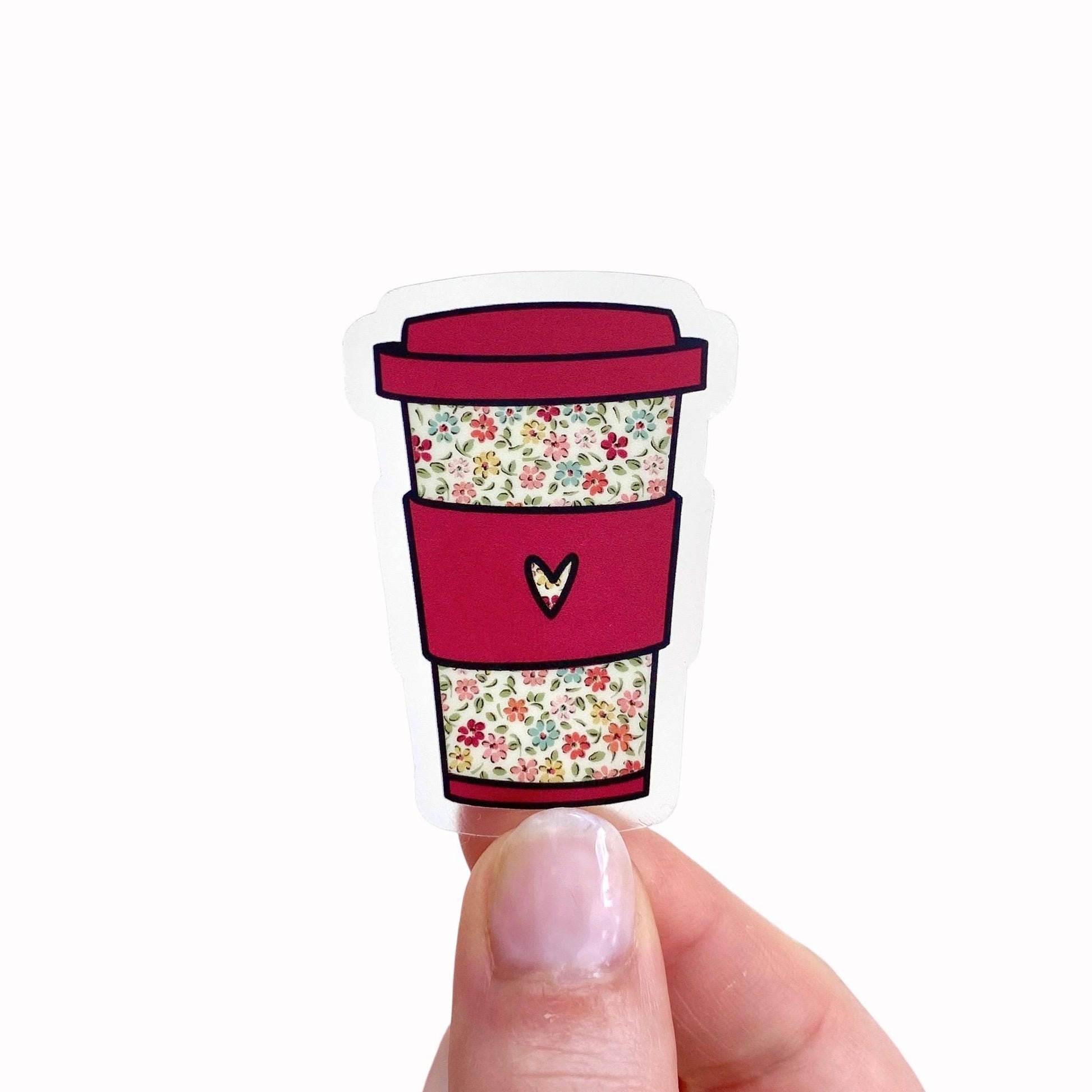 Sticker of a red coffee cup with floral pattern held between fingers on a white background
