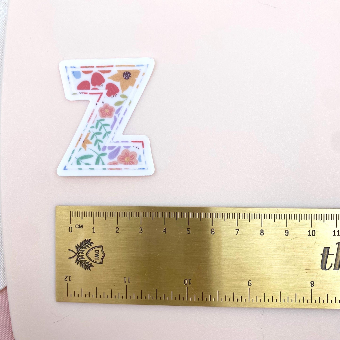 Decorative letter 'Z' sticker with floral patterns on a white background with a gold ruler for scale.