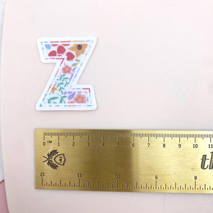 Decorative letter 'Z' sticker with floral patterns on a white background with a gold ruler for scale.