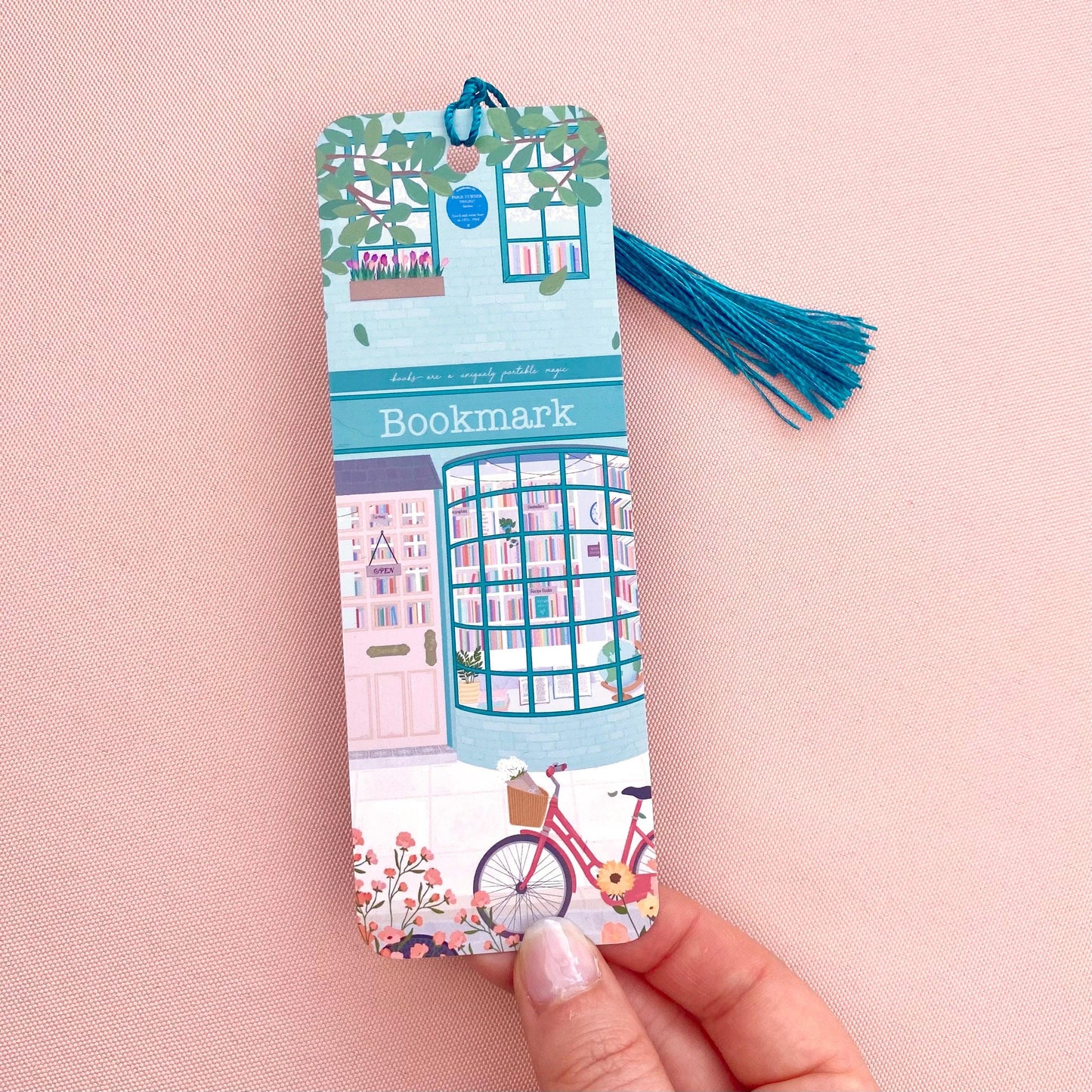 Bookshop illustration bookmark with tassel held by a hand on a pink background