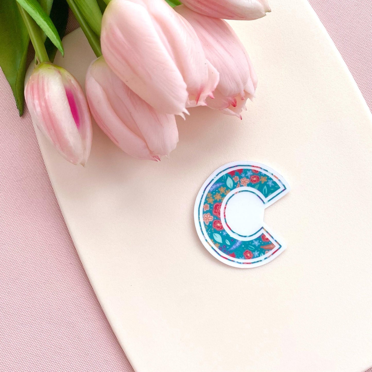Floral-patterned letter 'C' sticker on a pink surface with pink tulips