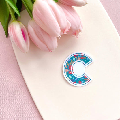 Floral-patterned letter 'C' sticker on a pink surface with pink tulips