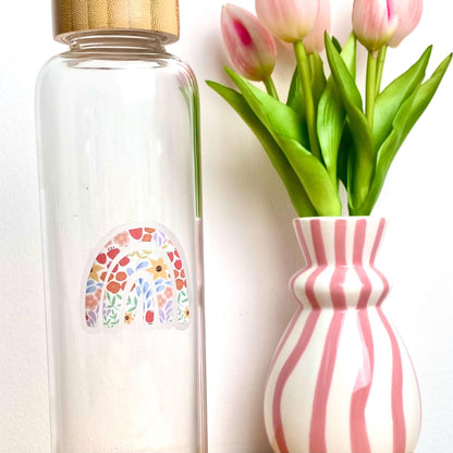 Clear water bottle with a floral patterned rainbow sticker next to a pink and white striped vase with tulips.