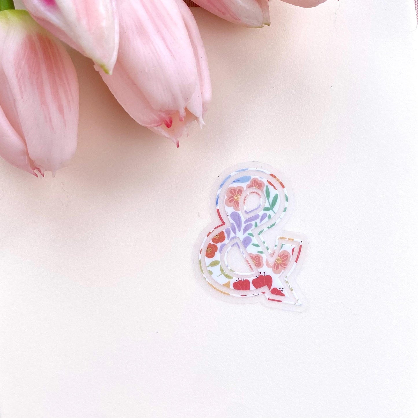 Decorative symbol'&' sticker with floral elements on a light pink background with tulips.