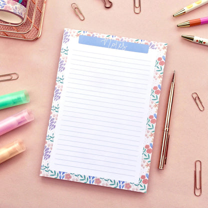 Floral border notepad with stationery items on a pink surface